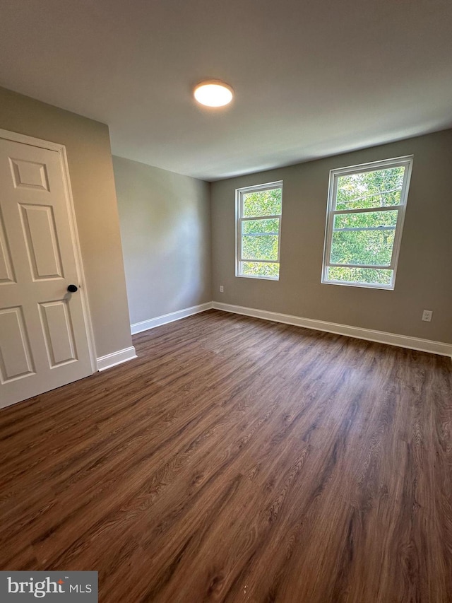 unfurnished room with baseboards and dark wood-type flooring