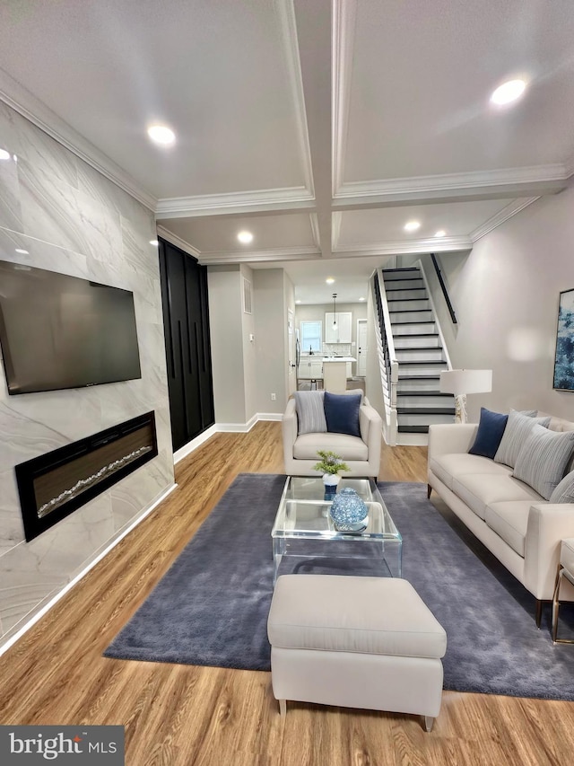 living room featuring a high end fireplace, coffered ceiling, stairway, and wood finished floors