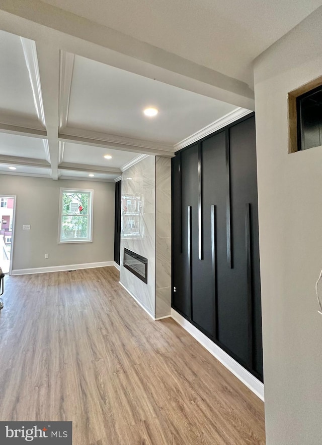 unfurnished living room featuring beam ceiling, light wood finished floors, a high end fireplace, coffered ceiling, and baseboards