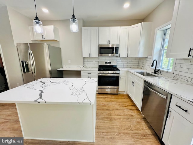 kitchen with stainless steel appliances, a kitchen island, a sink, white cabinetry, and hanging light fixtures