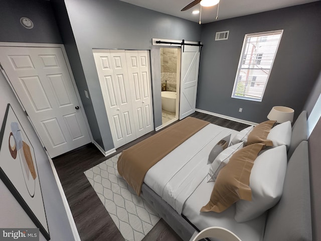 bedroom with ceiling fan, a barn door, dark wood-type flooring, and connected bathroom