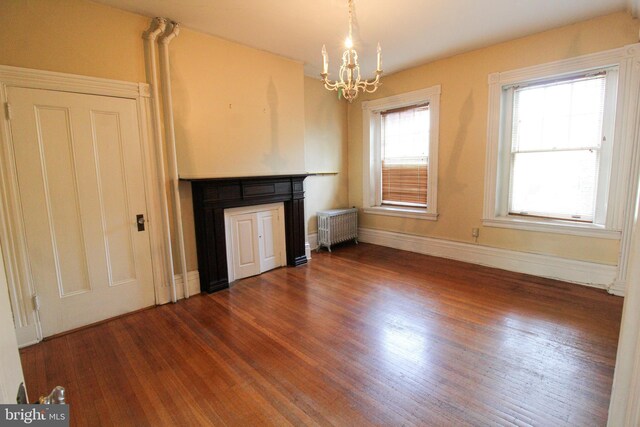 unfurnished living room featuring radiator, a notable chandelier, and dark wood-type flooring