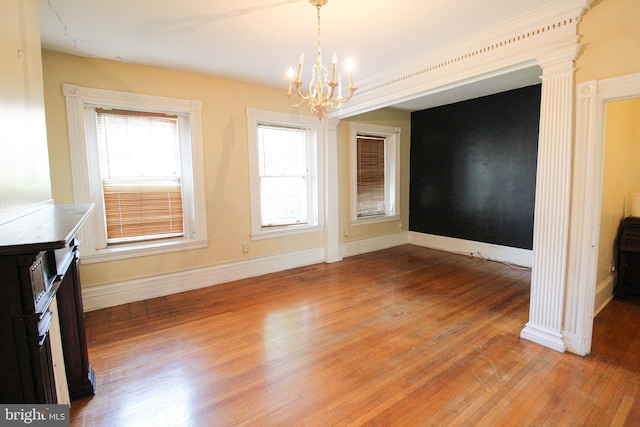 unfurnished dining area featuring ornate columns, wood-type flooring, plenty of natural light, and an inviting chandelier