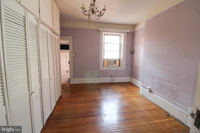 unfurnished bedroom featuring cooling unit, hardwood / wood-style floors, a closet, and a chandelier