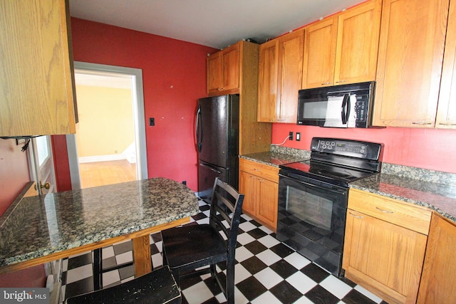 kitchen featuring a breakfast bar, dark stone counters, and black appliances