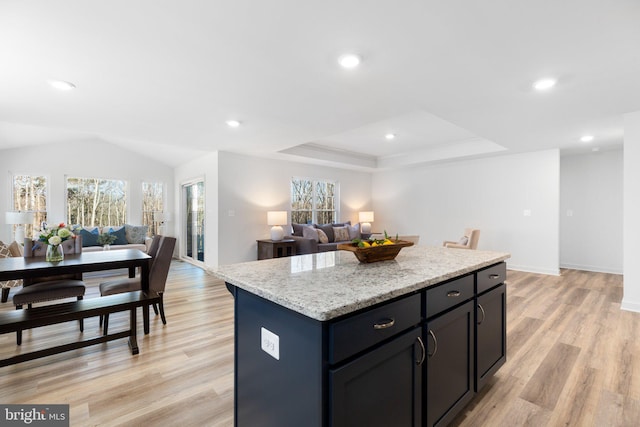 kitchen with light wood-type flooring, light stone counters, a center island, a tray ceiling, and lofted ceiling