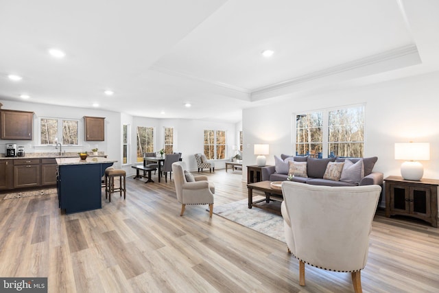 living room featuring ornamental molding, a tray ceiling, recessed lighting, and light wood-style floors