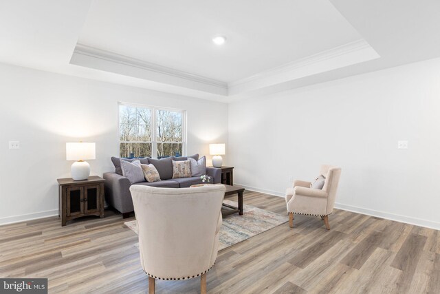 living room with a tray ceiling, crown molding, and light hardwood / wood-style flooring