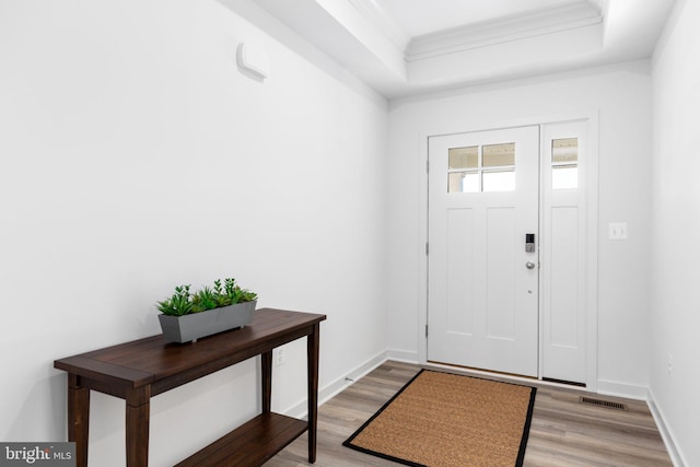 entrance foyer with visible vents, baseboards, ornamental molding, a tray ceiling, and light wood-style floors