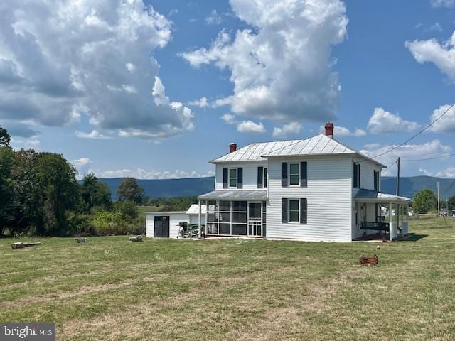 back of house with a standing seam roof, metal roof, a sunroom, a lawn, and a chimney