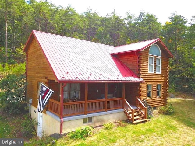 view of front of property featuring log siding, metal roof, covered porch, a standing seam roof, and a wooded view