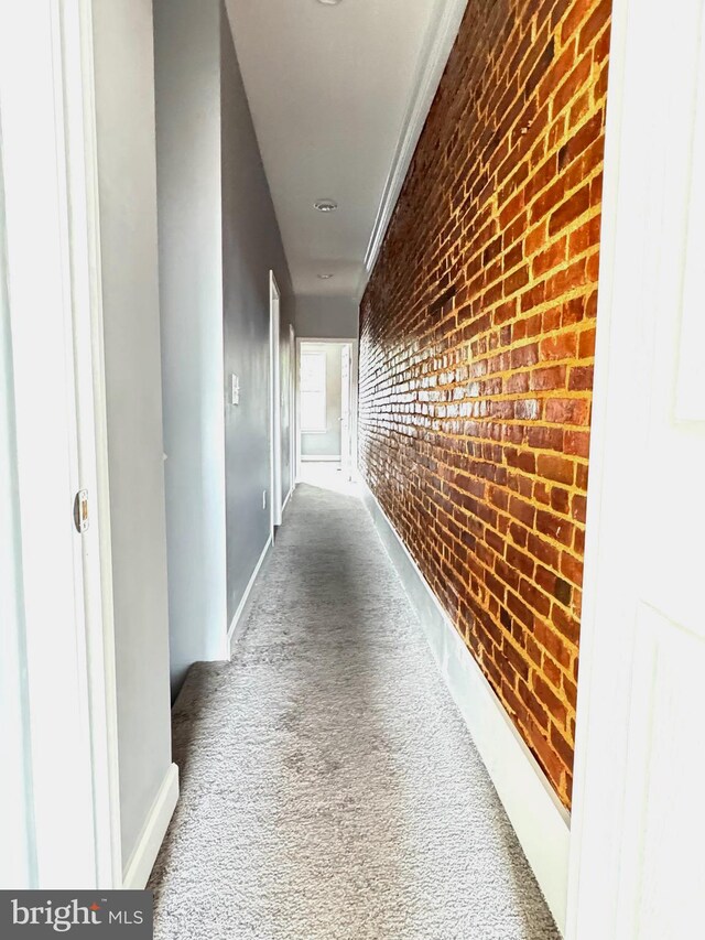 hall featuring brick wall, baseboards, an accent wall, and carpet