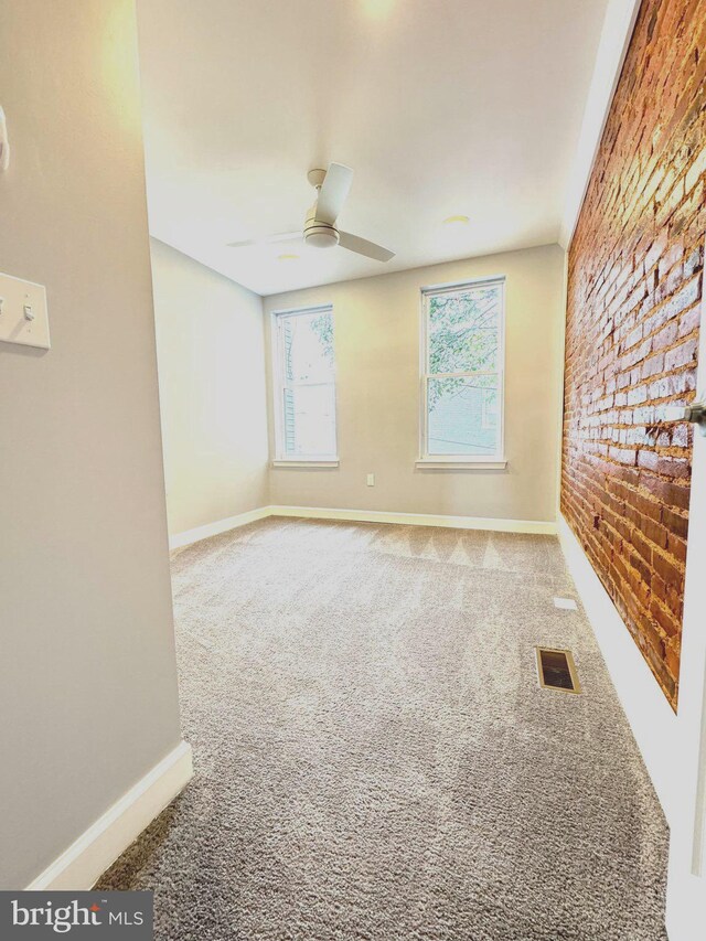 unfurnished room featuring visible vents, a ceiling fan, carpet floors, brick wall, and baseboards