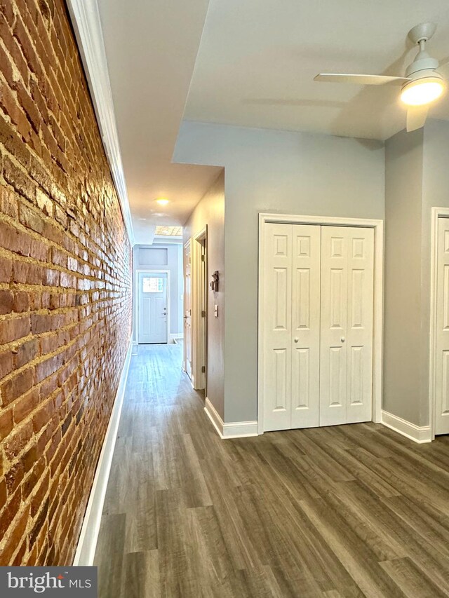 corridor featuring baseboards, dark wood-type flooring, and brick wall