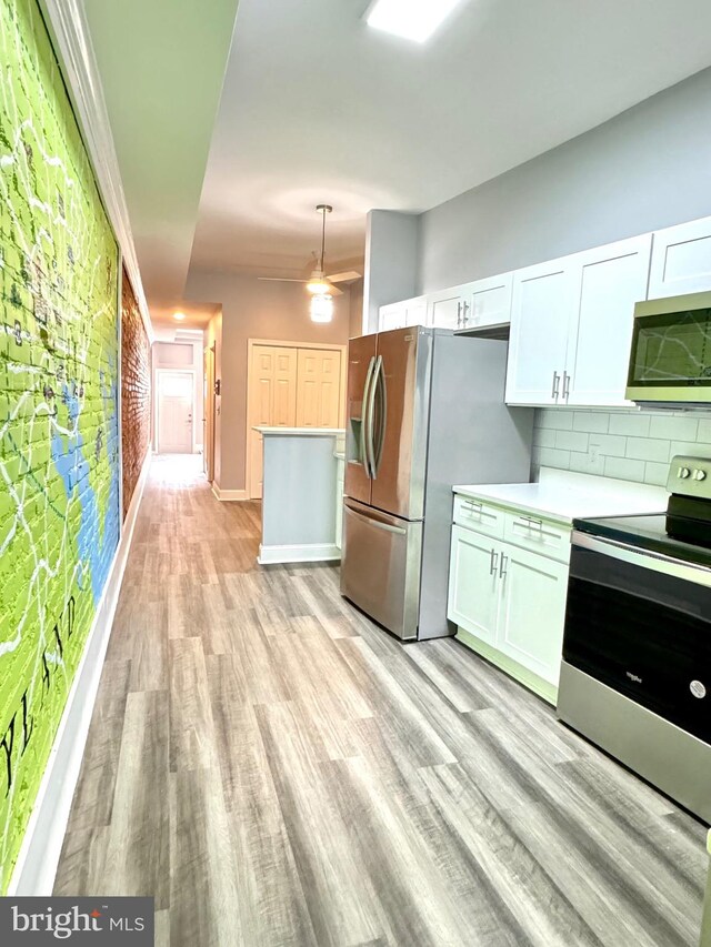 kitchen featuring light wood finished floors, light countertops, appliances with stainless steel finishes, white cabinetry, and backsplash