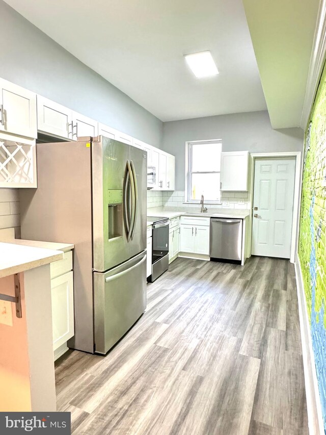 kitchen with light wood finished floors, light countertops, decorative backsplash, white cabinets, and stainless steel appliances