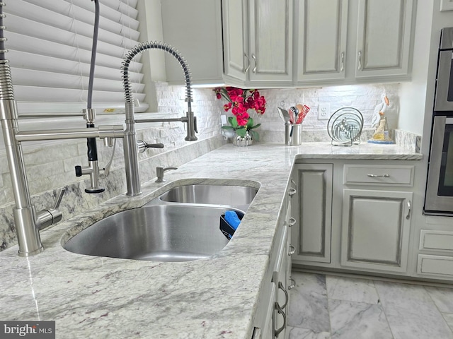 kitchen featuring tasteful backsplash, gray cabinets, sink, and light stone counters