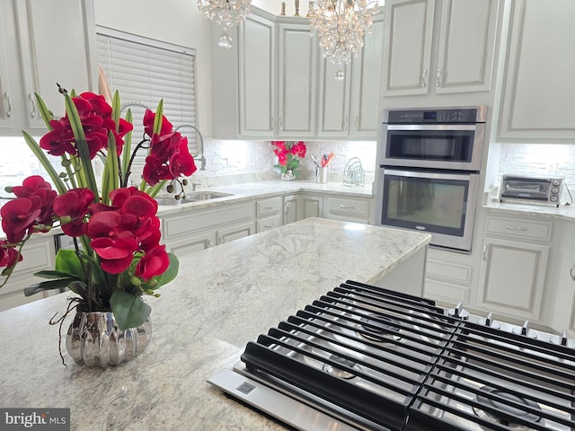 kitchen featuring sink, white cabinetry, an inviting chandelier, double oven, and backsplash