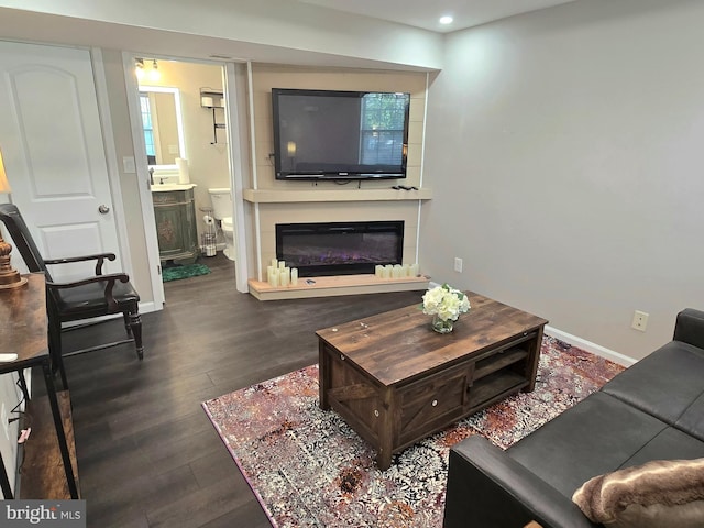 living area with a glass covered fireplace, dark wood-type flooring, baseboards, and recessed lighting