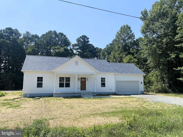 modern farmhouse featuring a shingled roof, gravel driveway, covered porch, an attached garage, and a front lawn