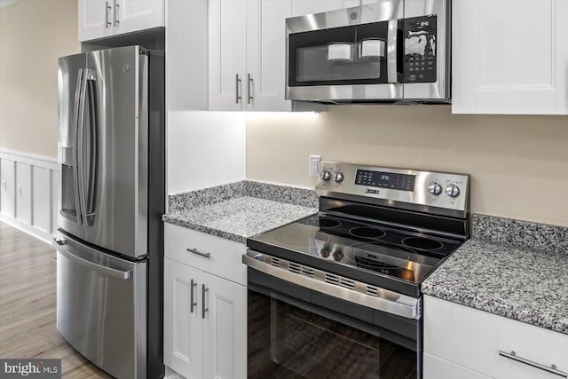 kitchen with stainless steel appliances, white cabinets, light wood-type flooring, and light stone countertops