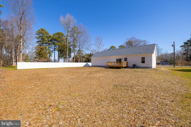 rear view of property with cooling unit, fence, a wooden deck, and a lawn