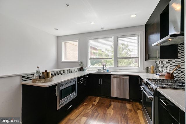 kitchen with wall chimney exhaust hood, dark wood-type flooring, stainless steel appliances, sink, and tasteful backsplash