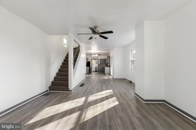 unfurnished living room with ceiling fan with notable chandelier and dark hardwood / wood-style flooring