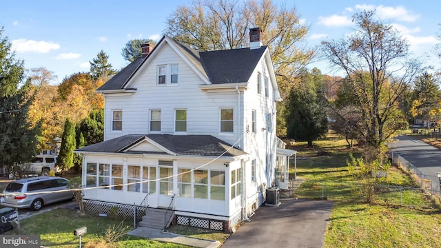 view of front of property featuring central air condition unit, a sunroom, and a front yard