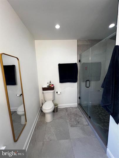 bathroom featuring a shower with door, tile patterned floors, and toilet