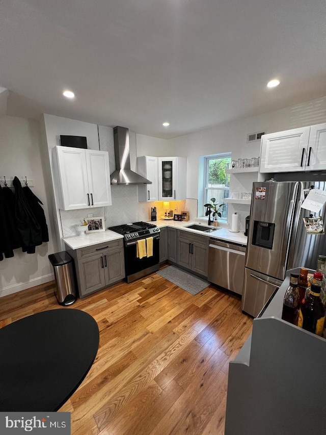 kitchen with light wood-type flooring, gray cabinets, appliances with stainless steel finishes, white cabinets, and wall chimney range hood