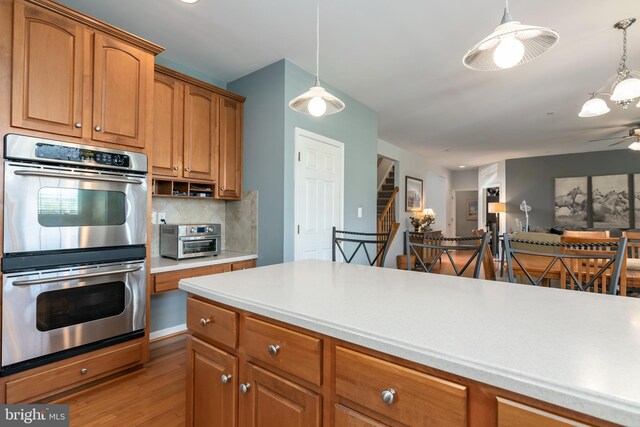 kitchen with ceiling fan, light wood-type flooring, decorative backsplash, decorative light fixtures, and double oven