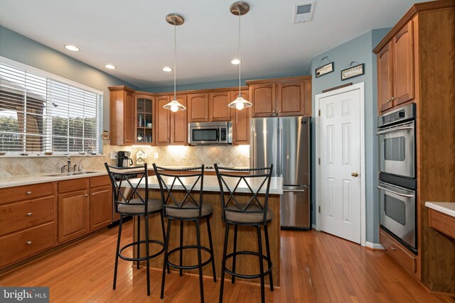 kitchen featuring decorative backsplash, light wood-type flooring, appliances with stainless steel finishes, decorative light fixtures, and a breakfast bar area