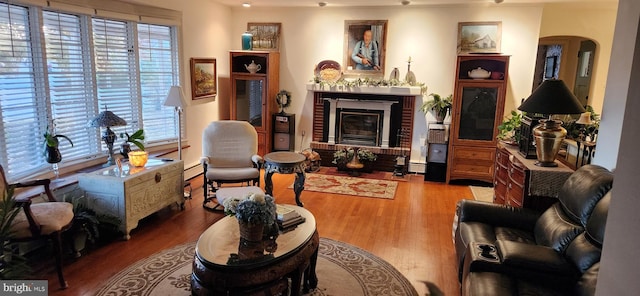 living area featuring arched walkways, a baseboard radiator, a fireplace, and wood finished floors