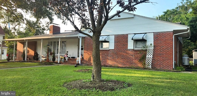 view of front of property featuring covered porch, brick siding, a front lawn, and a chimney