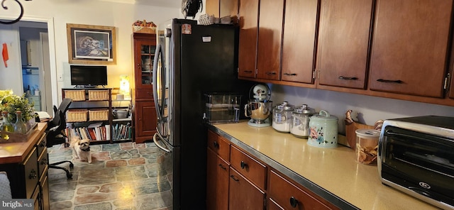 kitchen featuring stone finish flooring, a toaster, brown cabinets, and freestanding refrigerator