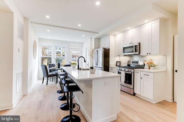 kitchen with a kitchen island with sink, appliances with stainless steel finishes, white cabinetry, and a kitchen bar