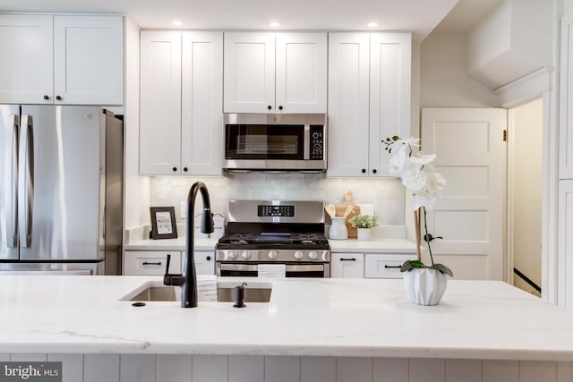 kitchen with light stone countertops, appliances with stainless steel finishes, white cabinetry, and decorative backsplash