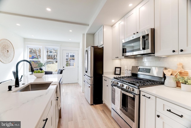 kitchen with light wood-type flooring, white cabinets, appliances with stainless steel finishes, and sink