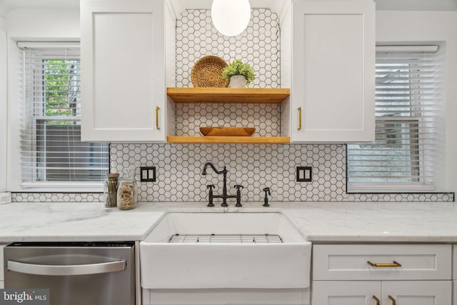 kitchen featuring light stone countertops, backsplash, stainless steel dishwasher, and white cabinets