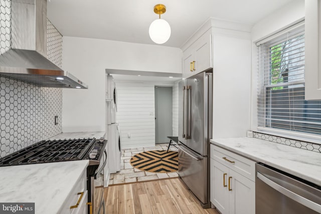 kitchen with light hardwood / wood-style floors, tasteful backsplash, stainless steel appliances, wall chimney range hood, and white cabinets