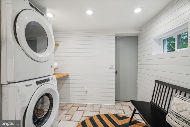 laundry room with wood walls and stacked washer / dryer