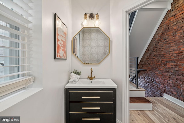 bathroom featuring brick wall, hardwood / wood-style floors, and vanity