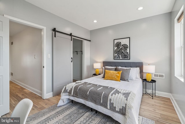 bedroom featuring a barn door, light wood-type flooring, and multiple windows