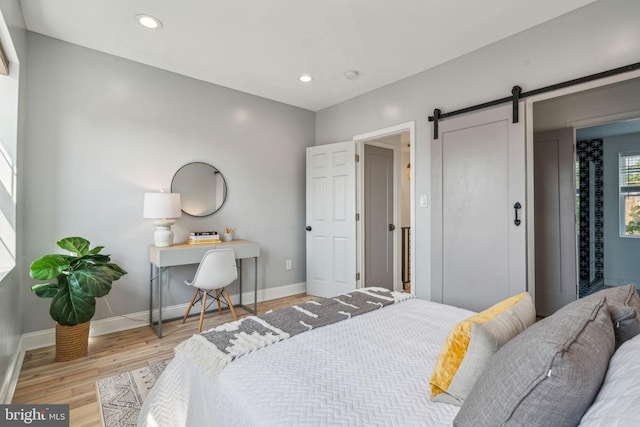 bedroom with a barn door and light wood-type flooring