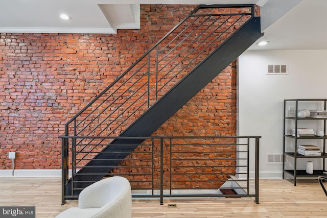 staircase with brick wall and hardwood / wood-style floors