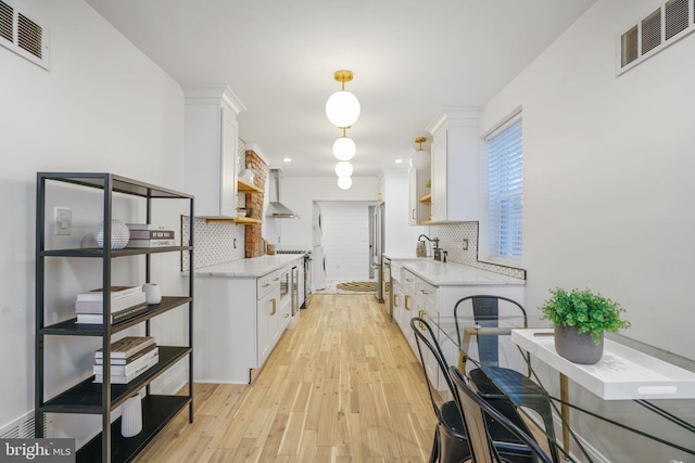 kitchen with light hardwood / wood-style floors, wall chimney exhaust hood, white cabinetry, and tasteful backsplash