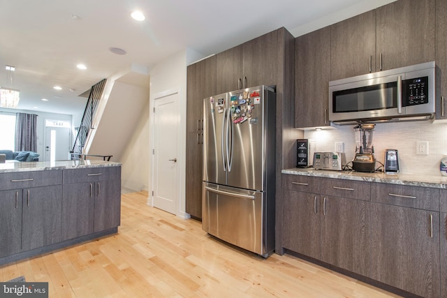 kitchen with light stone countertops, light wood-type flooring, stainless steel appliances, and decorative backsplash