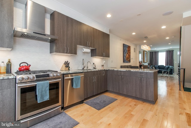 kitchen featuring appliances with stainless steel finishes, sink, light hardwood / wood-style flooring, light stone counters, and wall chimney exhaust hood