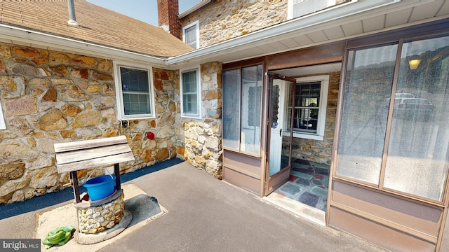 property entrance with stone siding, a shingled roof, a chimney, and a patio area